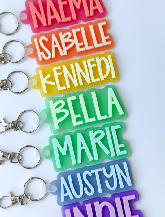 Personalized 3D printed name keychain made from colored plastic, showing a custom name in raised letters, attached to a metal keyring, placed on a plain background.
